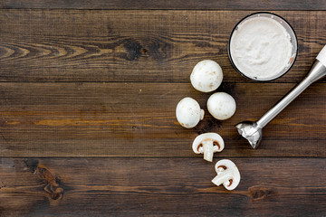 Cook cream soup with mushrooms. Champignon and blender on dark wooden background top view copy space