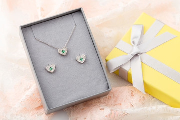 Jewelry set of heart necklace and stud earrings with white and green crystals in gift box on lace background
