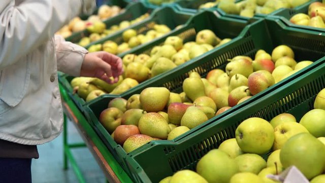 Someone selects pears in the supermarket. Female hand chooses green fruits in the vegetable department at the grocery store.