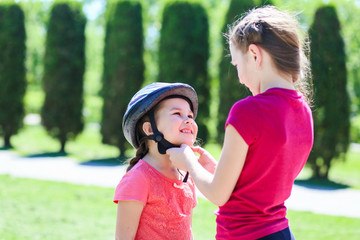 Fototapeta premium older sister wears a bicycle helmet to a younger sister