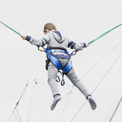 boy teenager jumps high to the sky insured with slings on an entertaining attraction.