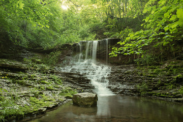 Obraz premium Beautiful mountain rainforest waterfall with fast flowing water and rocks, long exposure. Natural seasonal travel outdoor background in hipster vintage style