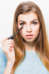 Gorgeous young woman with long hair and blue eyes applying makeup. Closeup, studio lighting retouched 