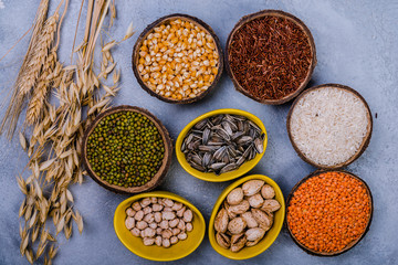 Assorted cereals, beans, seeds  in  bowls  on grey concrete table, flat-lay