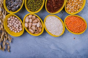 Assorted cereals, beans, seeds  in  bowls  on grey concrete table, flat-lay