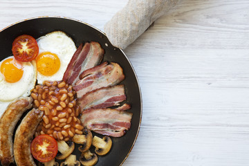 Full English Breakfast in cooking pan with sausages, fried eggs, beans and bacon on a white wooden background, top view. Copy space. From above. Flatlay.