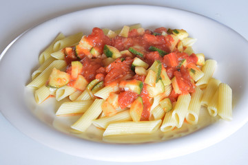 white plate full of penne pasta with tomato sauce and zucchini