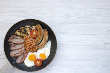 Full English Breakfast in cooking pan with sausages, fried eggs, beans and bacon on a white wooden background, top view. Copy space. From above. Flatlay.