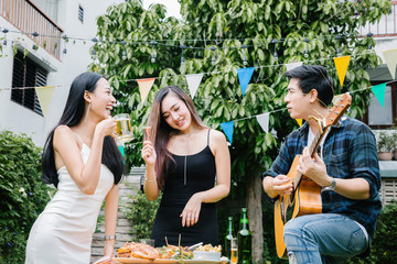 Group of friends having party in home garden.Happy young mates enjoying party playing guitar, singing and drinking beer eating food in garden.