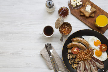 Full English breakfast in a pan with fried eggs, bacon, beans, sausages  and toasts on white wooden background, top view. Copy space. Flat lay. From above.