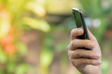 Close up of man hand holding smart phone with green nature background.
