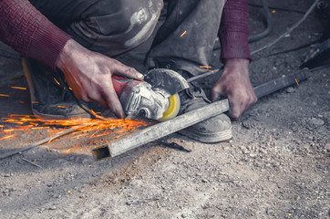 Manual cutting metal pipe with a circular saw. Hands, worker, flying sparks. - obrazy, fototapety, plakaty