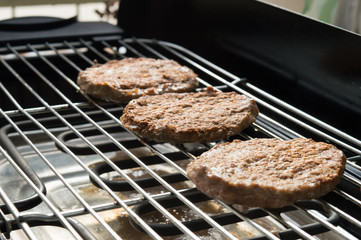 Three tasty meat hamburgers cooking on electric grill. A nice day to cook at the backyard