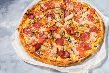Fresh homemade pizza with pepperoni, ham, cheese and tomato sauce on rustic concrete background.
