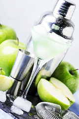 Alcoholic cocktail with green apple and dry vermouth, syrup, lemon juice and ice cubes. Bar tools, gray stone background, selective focus