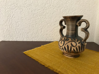 Brown jug on a wooden table in front of a white wall 