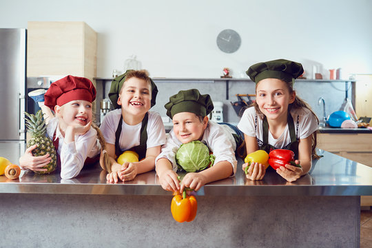 Funny children in the uniform of cooks on the table in vegetables in the kitchen.