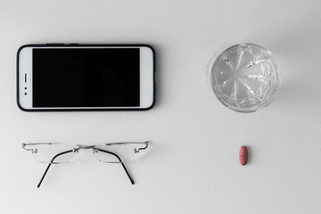 Unisex flatlay in a minimalist style with smart phone mock up, glasses, some pill and glass of water