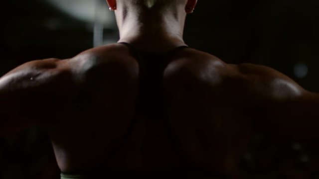 Rear view of muscular woman doing dumbbell lateral raise exercise in dark gym