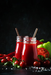 Healthy and useful spicy smoothies or juice from red tomatoes and bell peppers with green basil in glass bottles on a dark background, selective focus