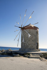 Fototapeta na wymiar Ancient windmills on stony Rhodes coastline in harbor, old historic buildings, place of interest, blue sky