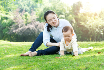 Happy mother and baby sitting on meadow in park