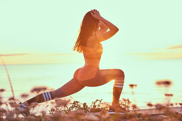 Fitness woman practicing stretching yoga exercises in nature against the background of a sea at sunset.