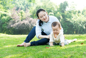 Naklejka na ściany i meble Happy mother and baby sitting on meadow in park