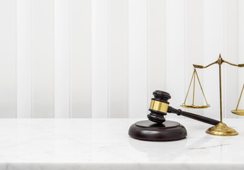 Wooden gavel and lawyer balance scales on white marble counter table top.