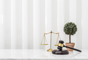Wooden gavel and lawyer balance scales on white marble counter table top.