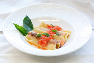 Italian cannelloni pasta with tomato sauce and basil on white ceramic plate