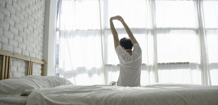 Men sit at the edge of the bed. And stretching his arms to relax in the morning.Wake up in the morning.Stretching after waking.