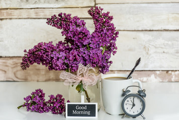 Fototapeta na wymiar Bouquet of Lilac with Alarm Clock,Cup of Coffee and Good Morning Text on Wooden Background .Spring Morning Concept