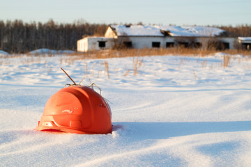 broken orange construction helmet on the background of a ruined building in a snowdrift