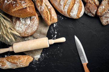 Different bread with flour and spikelets of wheaton black background