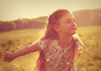Beautiful smiling kid girl trying to fly with happy look on nature bright sunset summer background....