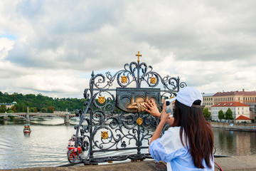 The girl touches the statue of St. John Nepomuk on Charles bridge Prague. The touch of a person to the memorial plaque of the Saint should bring good luck and ensure your well-being