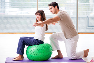 Personal coach helping woman in gym with stability ball