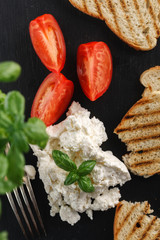 homemade ricotta cheese with toasts and tomato on black plate. Top view