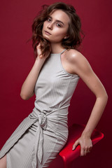 Fototapeta premium portrait of young girl in grey dress on red background sitting pose