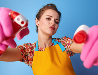 housewife using bottles of cleaning detergent as guns on blue
