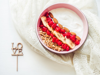 Word LOVE, berry smoothie, muesli with nuts, dry berries, pieces of banana in a pink plate on a stylish table. Close up, top view. Concept of healthy and delicious food