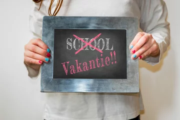 Fototapeten Child holding up a blackboard with word school crossed out and replaced with the Dutch word for holiday (vakantie) © Erik_AJV