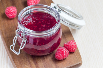 Raspberry jam in glass jar on a wooden board, horizontal, copy space