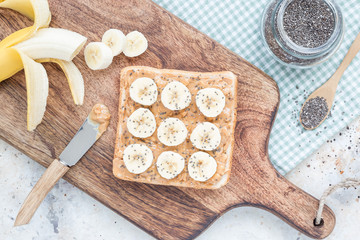 Healthy sandwich with crunchy peanut butter, banana and chia seeds, on a wooden board, ingredients on background, top view, horizontal