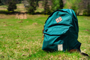 green tourist backpack  on a lawn background in the mountains, travel concept in the wild, copy space, closeup