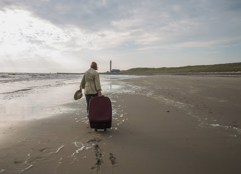 Attractive woman with a large suitcase walks along empty beach of the sea towards the horizon