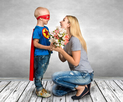 The son in the costume of a superhero gives his mother a bouquet of flowers.