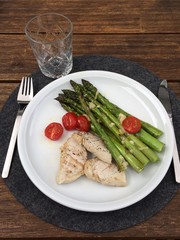 Green asparagus with chicken and cherry tomatoes on a plate with a knife and fork.
