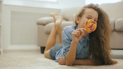 Beautiful fair-haired teen girl with Candy. Playful Cute Girl with Big Sweet Lollipop near sofa in front of a window. - Powered by Adobe